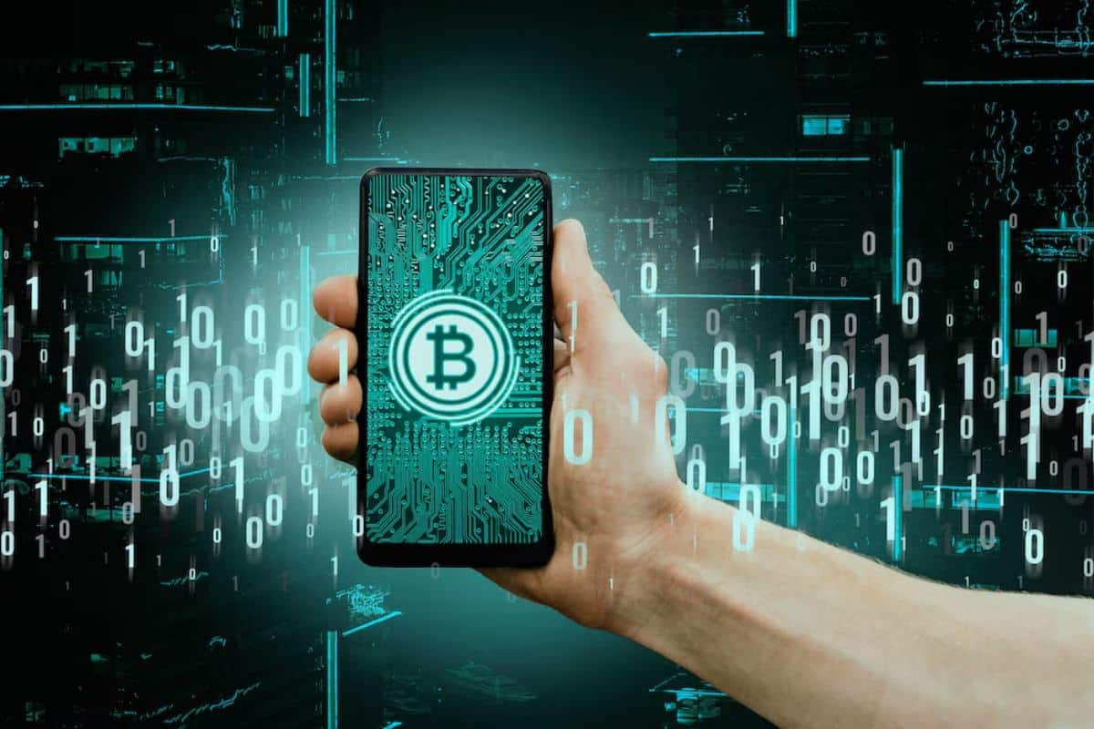 Hand holding a smartphone displaying a Bitcoin symbol on a circuit board background with glowing digital numbers.