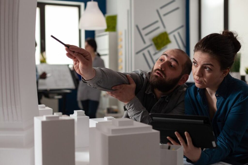 Two architects discussing over a model building layout in an office setting.