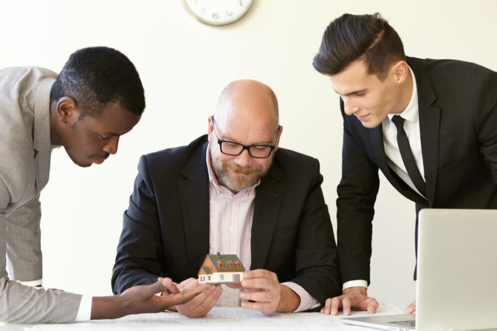Three people at a table with documents, one person signing papers with keys visible on the table.